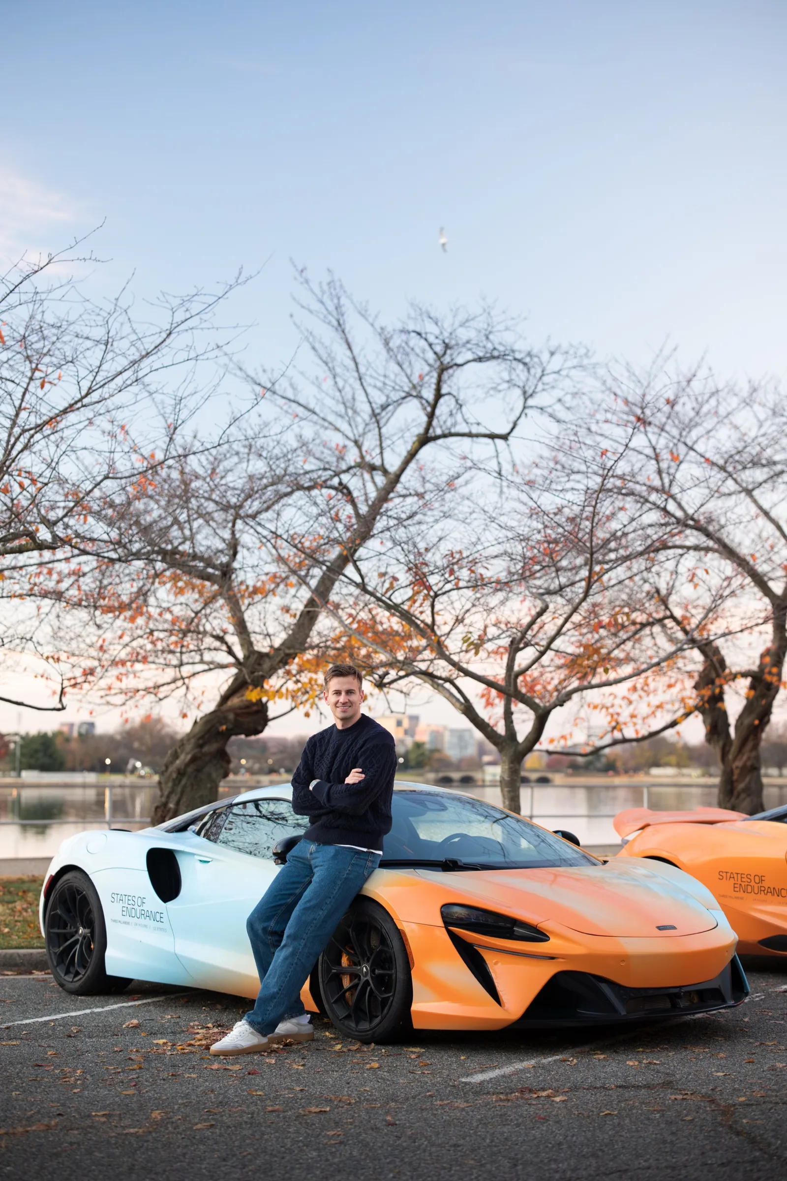 Jack Barlow, arms folded, leaning against a McLaren Artura in States of Endurance livery beside a river