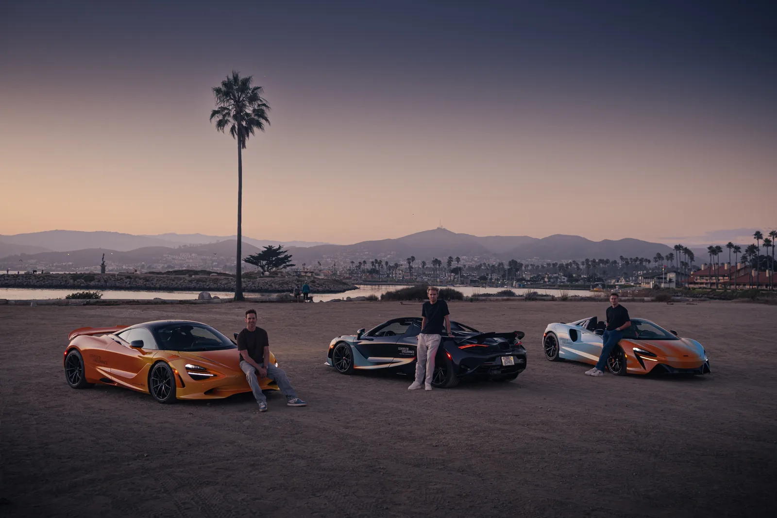 Three McLarens in States of Endurance livery on a beach at dusk, with the three drivers sitting on them, Jack Barlow on the right