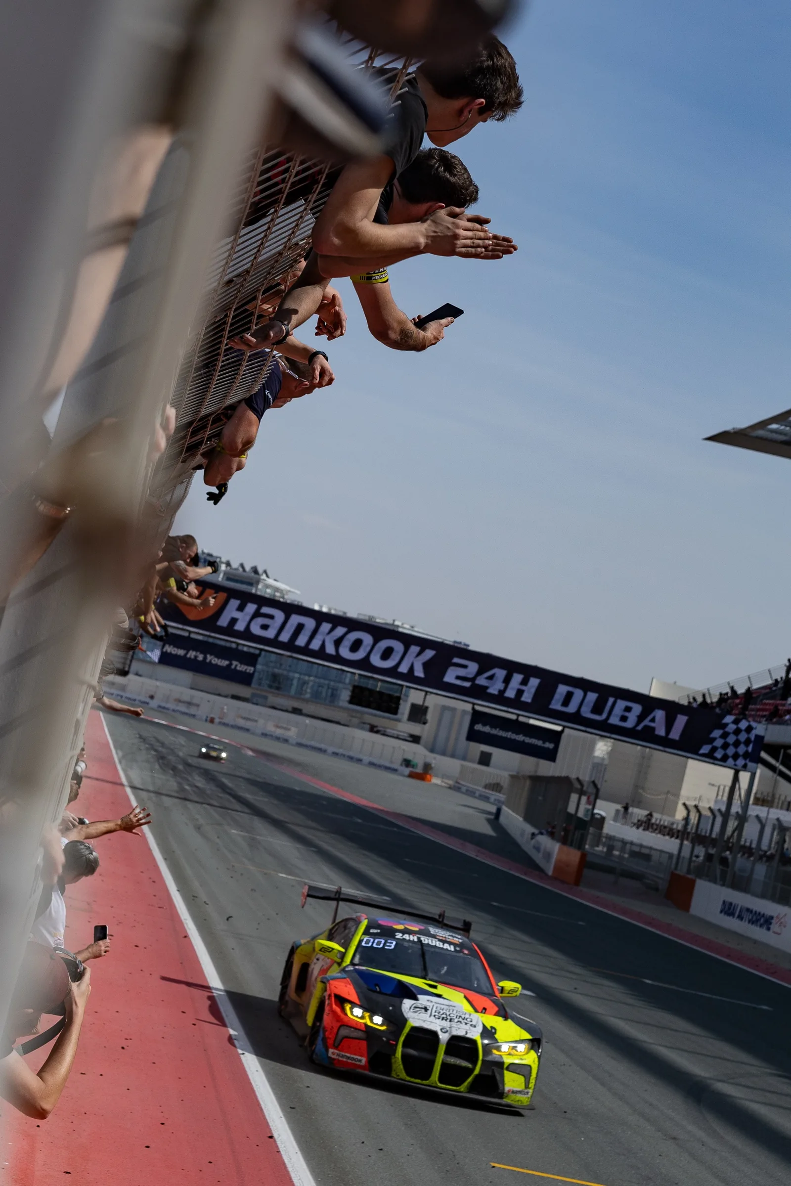 The BMW M4 GT3 crossing the line at the Hankook 24H Dubai as the team cheers from the pit wall