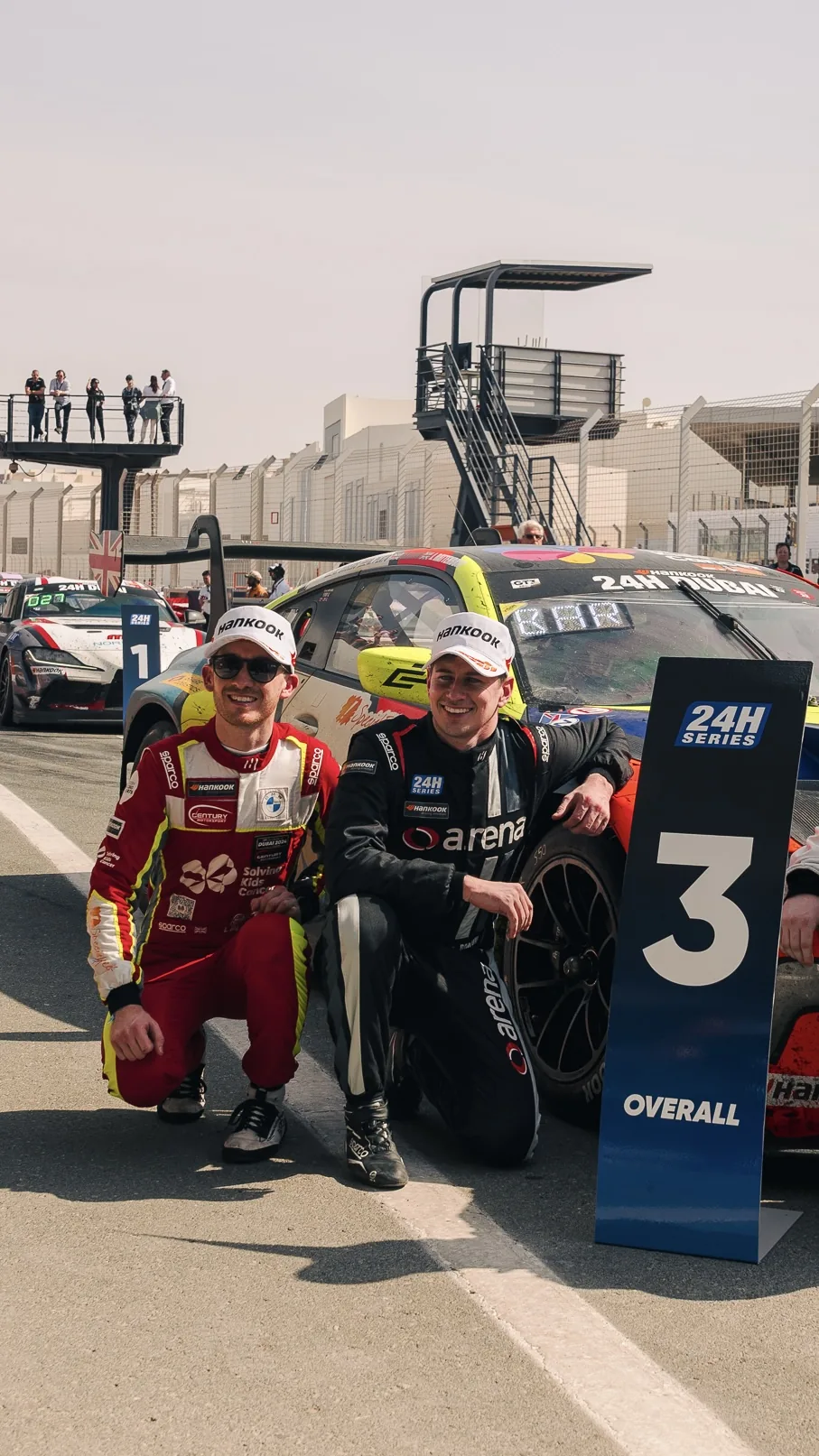 Jack Barlow and his co-driver kneeling beside the third-overall board after the 24H Dubai
