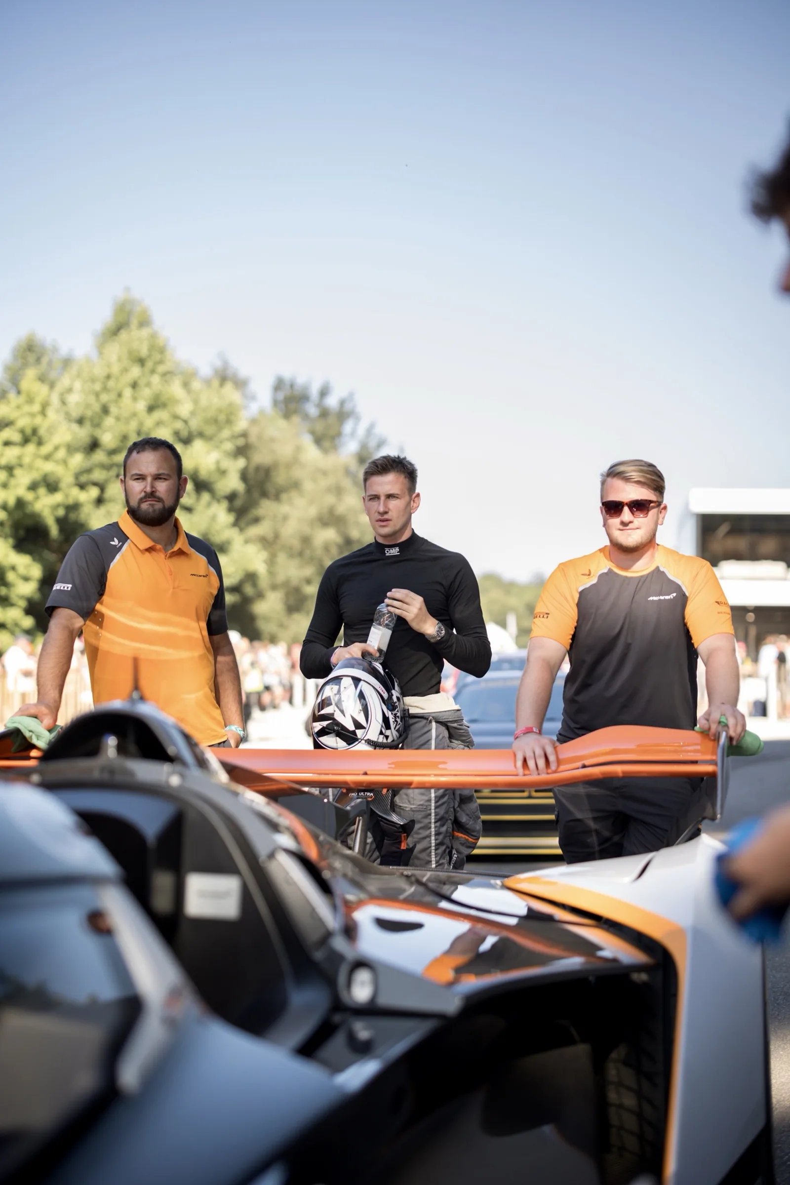 Jack Barlow, helmet in hand, with two McLaren crew members behind the rear wing of the Solus GT at Goodwood